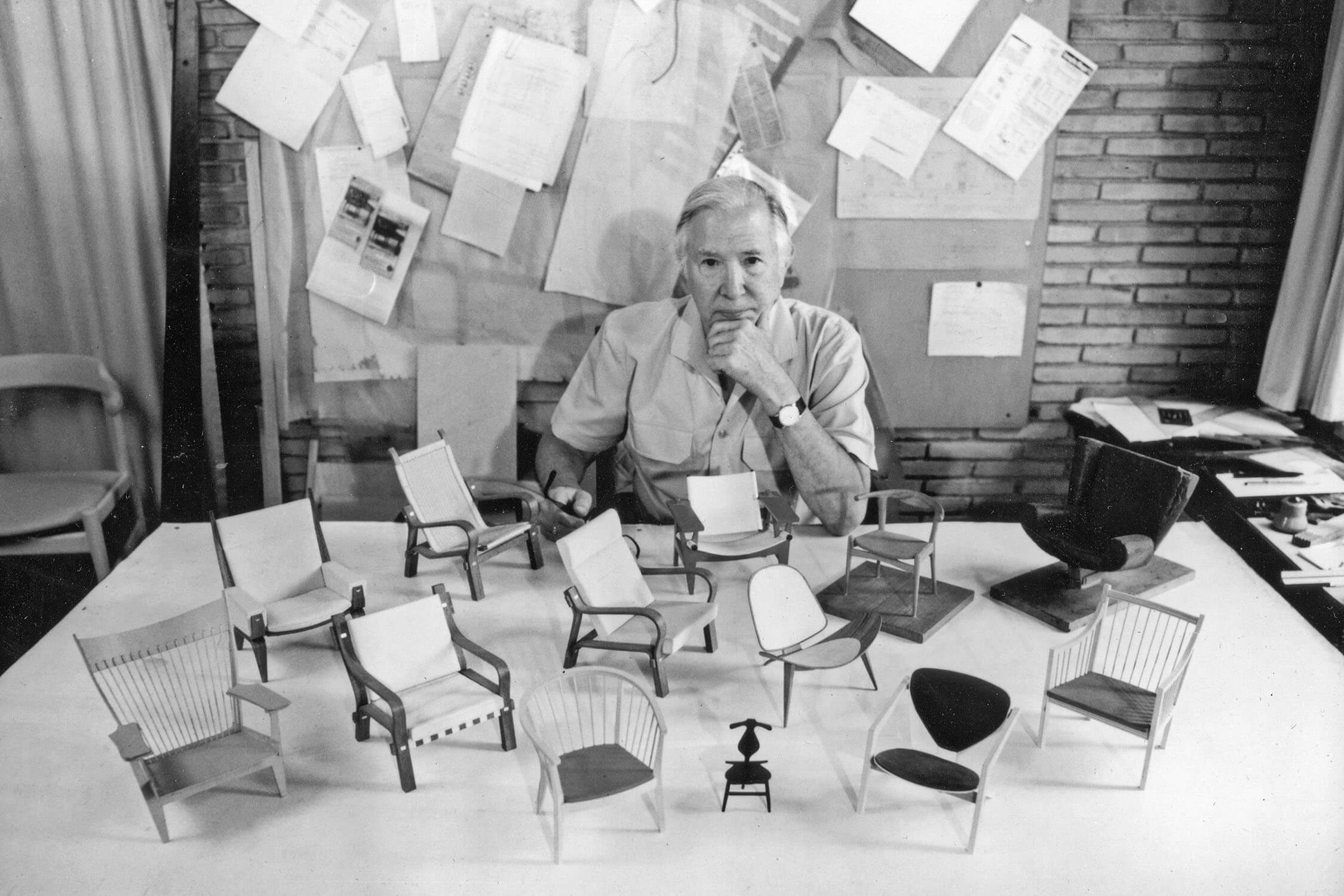 Designer Hans J. Wegner with chair models spread on a table in front of him